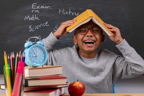 Cheerful thoughtful school boy, back to school concept. Stationery supplies on classroom desk with chalkboard background.